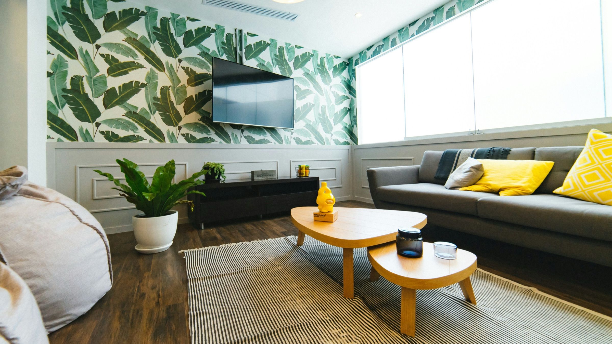 Living room with a dark sofa, yellow cushions and leaf-print wallpaper