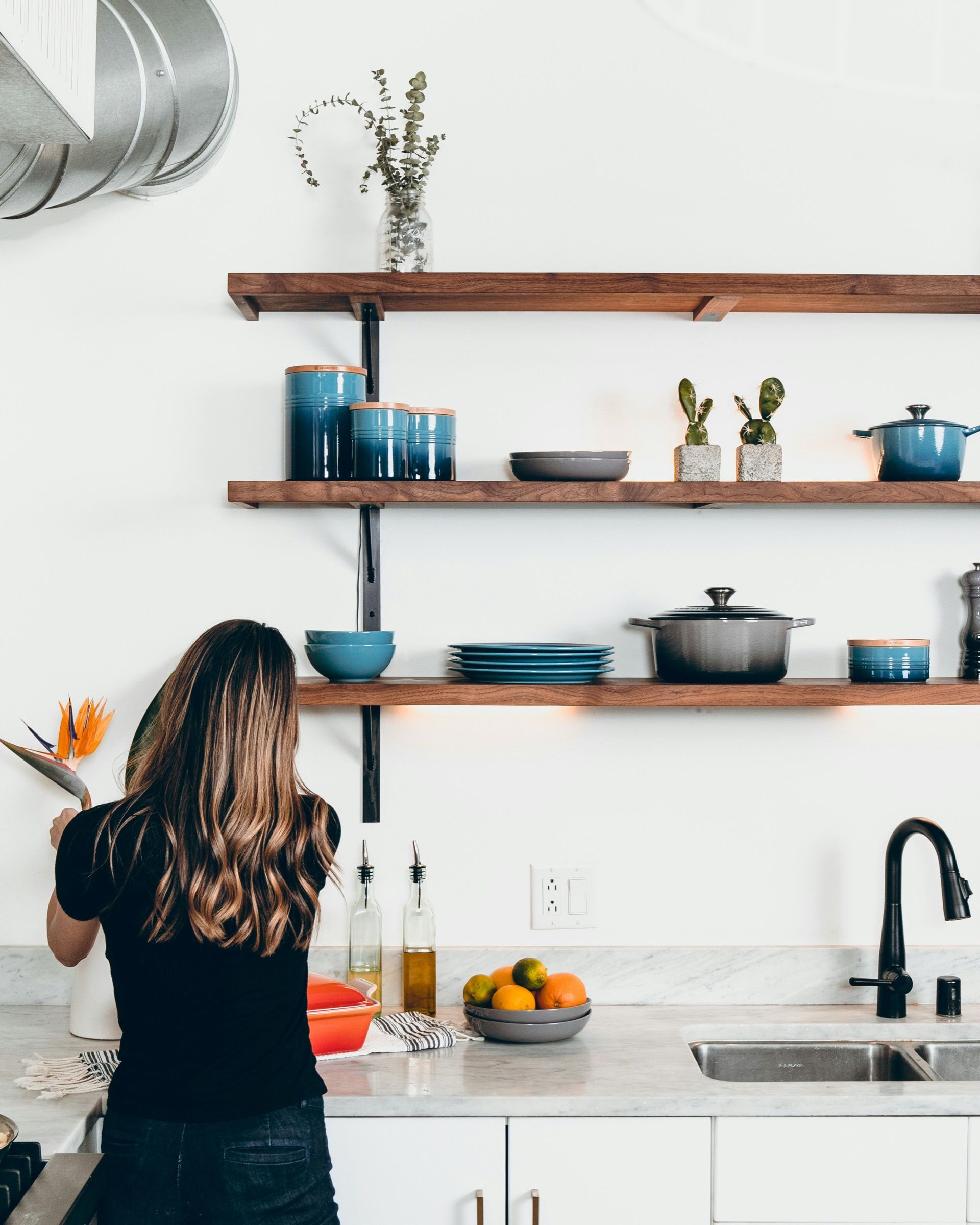 A woman reaching for a pan on open kitchen shelves above a white worktop