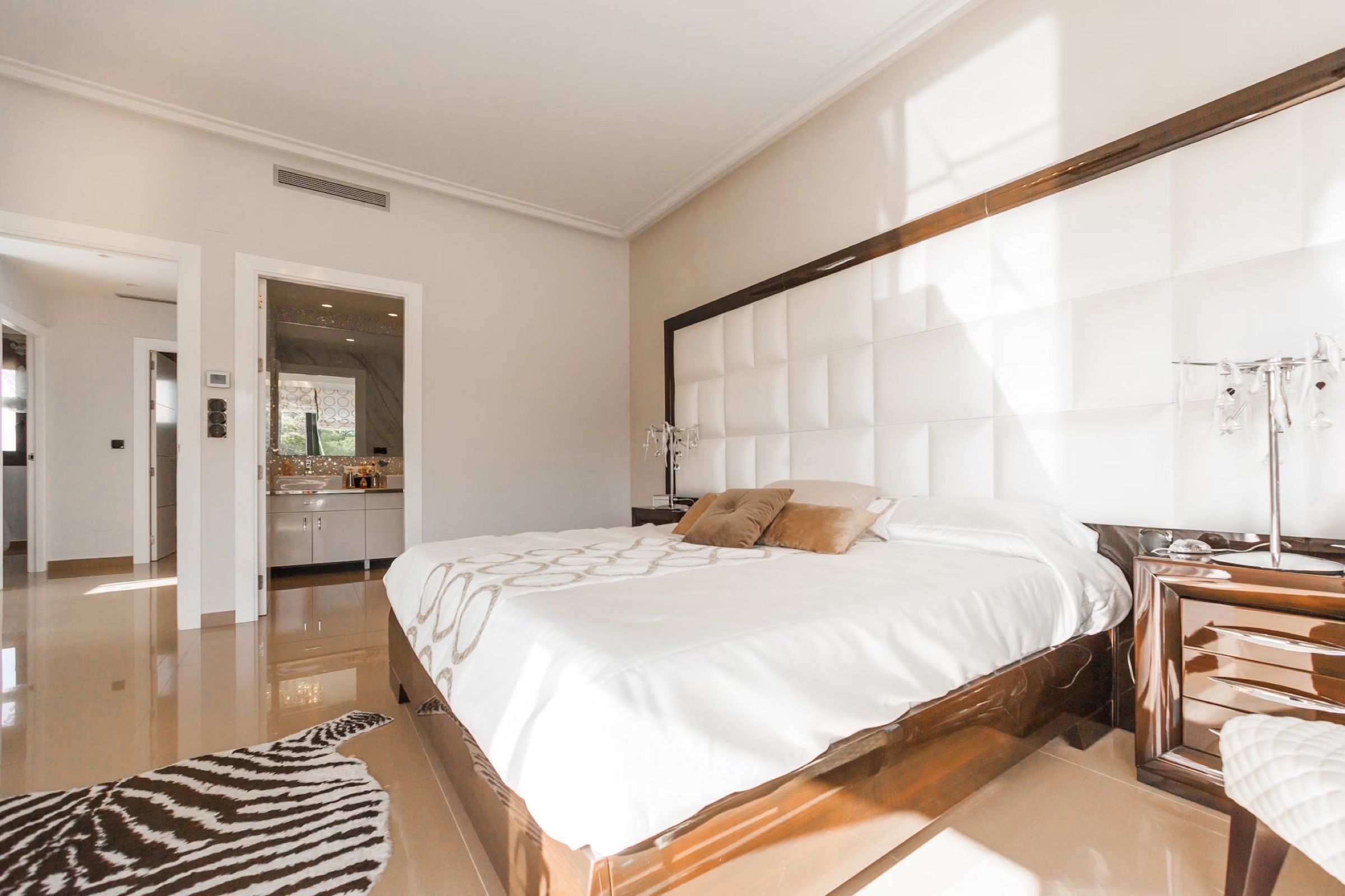 Bedroom with a large padded headboard, white bedding and a zebra-print rug
