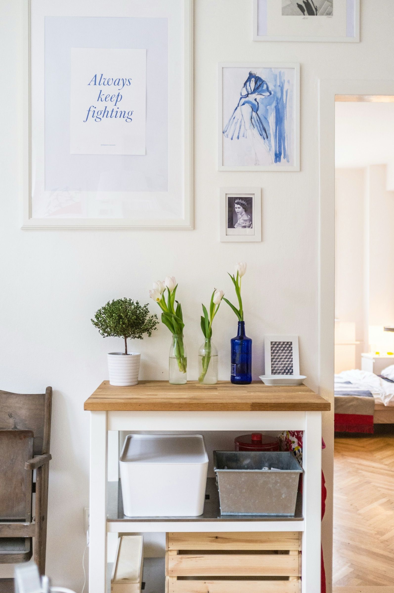 A small wooden kitchen trolley with plants and vases in front of framed prints